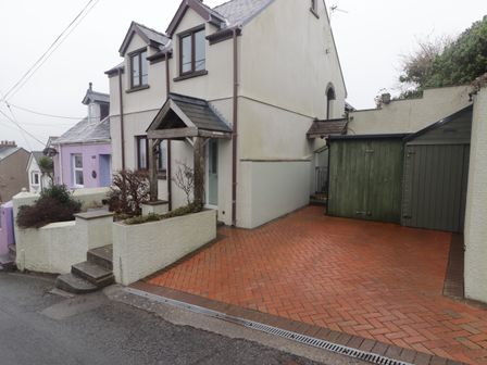 A driveway with two green storage sheds next to a two-story house with a porch at Cheriton in Pembroke Dock