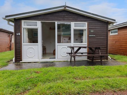 A small cabin with a picnic table outside and grass in front at Constantine Bay near St Merryn