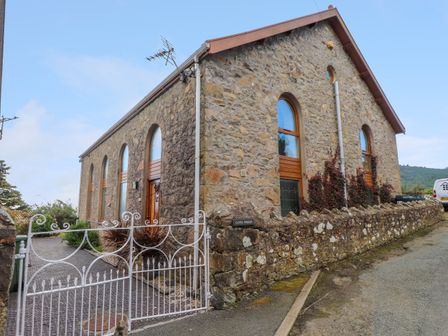 A stone building with arched windows and a white metal gate at Ty Capel Pisgah in Nefyn