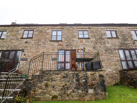 A stone cottage exterior with stairs and a balcony with outdoor furniture at Valley Cottage in Penzance