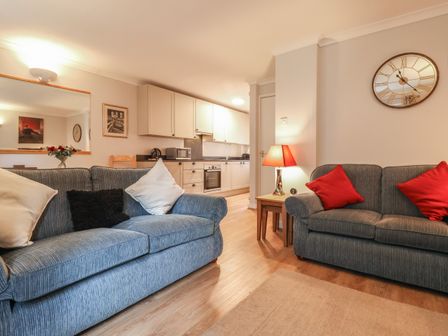 A living room with two sofas with cushions a side table lamp and a kitchen in the background at New Tower House- 10 Pear Tree Court in York