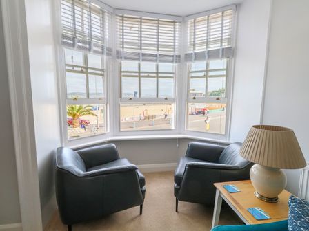 A corner seating area with two black armchairs near bay windows and a side table with a lamp at Two @ No36 in Weymouth