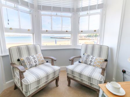 Two armchairs with striped cushions by bay windows overlooking a beach at Three @ No36 in Weymouth
