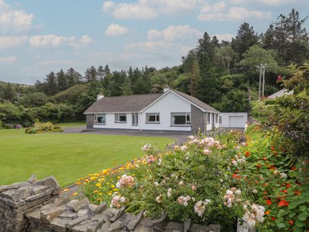 A single story house with a surrounding lawn and flower garden in front at Nellys House in Gortahork County Donegal