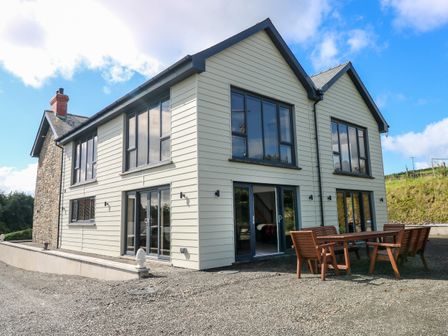 A two-story house with large windows and an outdoor wooden dining set on a gravel area at Little Pale Near Whitland