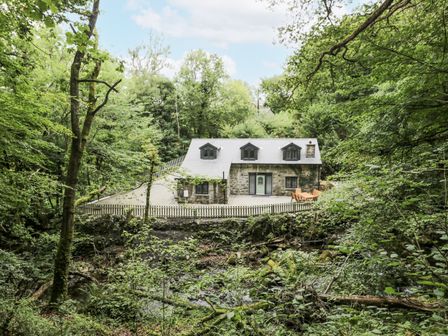 A house with a deck and fence surrounded by trees at Frongoch Old Power House in Dolgellau