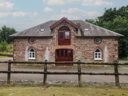 A stone building with arched windows and red doors behind a wooden fence at Meadow Cottage in Llanarthney nr Llandeilo Carmarthenshire