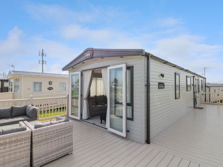 An exterior view of a mobile home with open patio doors a seating area on the deck at Drake 11 in Cayton Bay