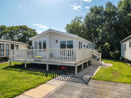 A white mobile home with a fenced deck and steps surrounded by grass and trees at 28 Finch in Cayton Bay
