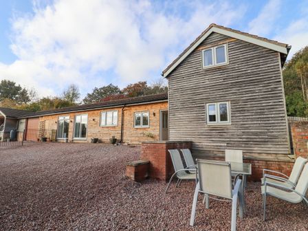 An outdoor patio area with a table and chairs next to a wooden house at Robins Rest in Gorsley