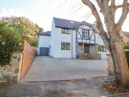 A large two-story house with a paved driveway and a tree in front at Hafan Y Mor in Prestatyn