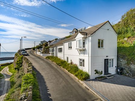 A white two-story house beside a narrow road near the coast with parked cars and a bicycle at Fairwinds in Portreath