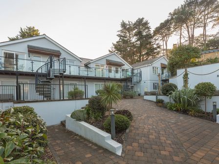 An exterior view of white buildings with balconies and spiral staircases surrounded by paved walkways and landscaped plants at 22 Bolt Head Near Salcombe
