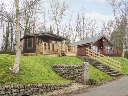 Two wooden lodges on a grassy slope with stone retaining walls and stairs at Park View Lodge Arnside 7 South Lakeland Leisure Village near Carnforth