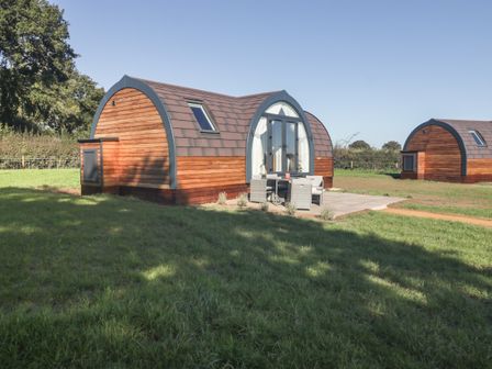 Two wooden arched cabins with patio furniture outside on grassy land at Leadon View Oak in Upleadon near Newent