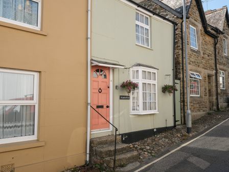 A street view of a row of houses with a peach door and hanging flower baskets at 5 Bodmin Hill in Lostwithiel