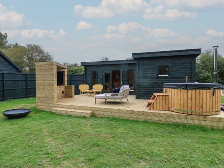 A wooden deck with outdoor seating a hot tub and a barbecue under a partly cloudy sky at Badger's Burrow in South Luffenham near Edith Weston