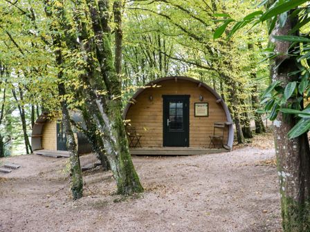 Two wooden pod cabins with curved roofs and black doors in a wooded area with trees and gravel ground at Ballybeg Pod 4 Ballybeg near Tinahely County Wicklow