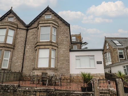 Stone two-story building with bay windows and white shutters with outdoor seating area behind iron fence at 5 Lyonesse Apartments in St Ives