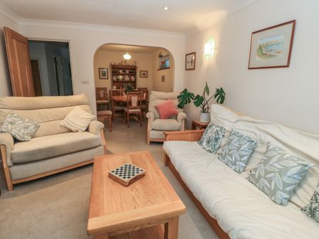 A living room with beige sofas pillows a wooden coffee table and a dining area with table chairs at Old Harry Cottage 16 Swanage