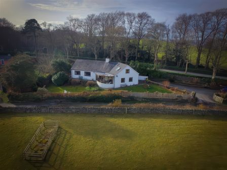 A single-story white house with a garden surrounded by trees and a green field at Artists Cottage in Minffordd near Penrhyndeudraeth