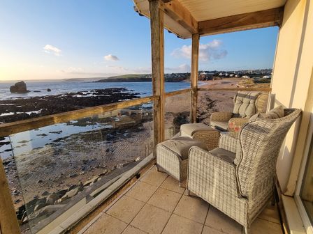 A balcony with chairs and a table overlooking the sea at Sea View Beach Apartment in Thurlestone