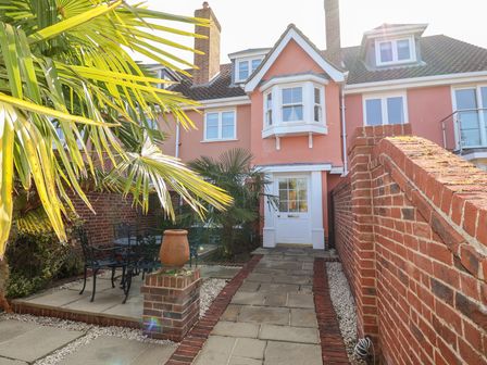 A courtyard with a patio area and outdoor furniture by a pink house with a bay window at 6 Willows Green in Aldeburgh