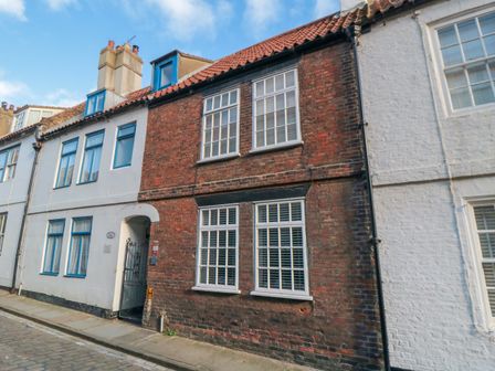 A row of attached brick and painted houses with windows and a gated entrance on a cobblestone street at Henrietta cottage in Whitby
