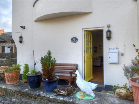 An outdoor area with potted plants a wooden bench a yellow door and a white duck statue at Radium in Lyme Regis