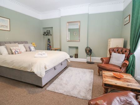 A bedroom with a double bed pillows a rug armchairs a wooden coffee table and a fan at Flat 1 St Agnes House Lyme Regis