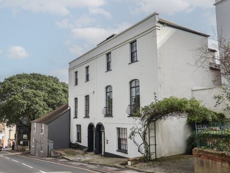 A street view of a white three story building with black windows and doors near a tree and an archway covered with plants at Flat 2 St Agnes House Lyme Regis