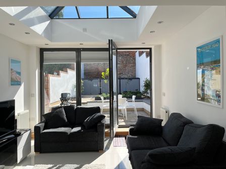 A living room with two black sofas a television and a glass door leading to an outdoor patio at 23 Millhams Street Christchurch