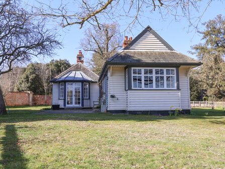 A house with white wooden siding and multiple windows surrounded by trees and grass at Holm Oak Lodge in Tendring near Weeley