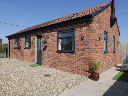 A brick house with black framed windows and a black door with hanging flower baskets and a potted plant by the pathway at Ashtree Cottage in Ottringham