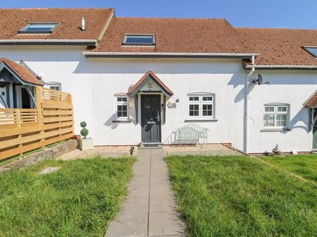 A white house with a tiled roof and front door with a small porch and paved path leading to it at The Cwtch in Aberporth