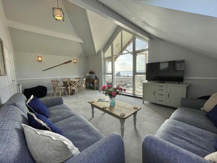 A living room with two sofas a coffee table a dining table and large windows with a sea view at 12 Thurlestone Rock in Thurlestone