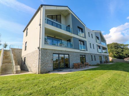 A three story building with stone and siding exterior and balconies overlooking a grassy area at 2 The Dunes in Falmouth
