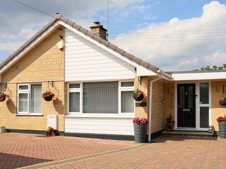 Exterior view of a house with hanging flower baskets and a black front door at Howard Cottage in North Littleton near Offenham