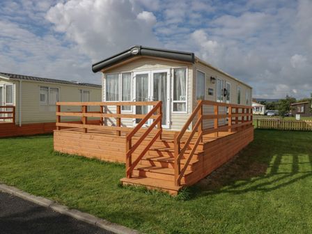 A mobile home with a wooden deck and steps on a grassy lawn at Elm in Denny