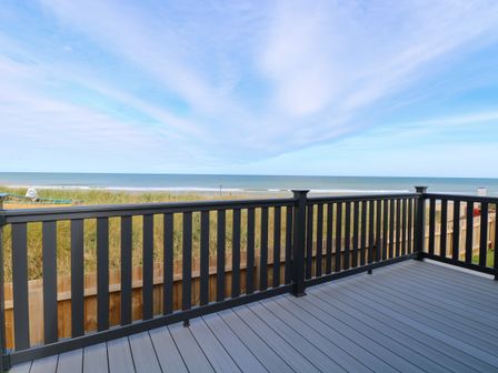 A deck with black railing overlooking grassy dunes and a beach at Seaview Lodge in Bacton