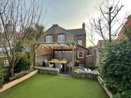 A backyard with a wooden pergola and dining table surrounded by chairs at Happy Place in Sheringham