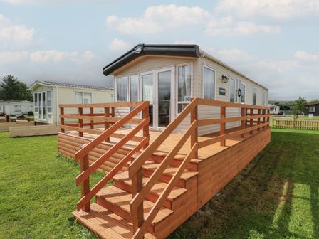 A mobile home with a wooden deck and stairs on a grassy area at Hazel in Denny