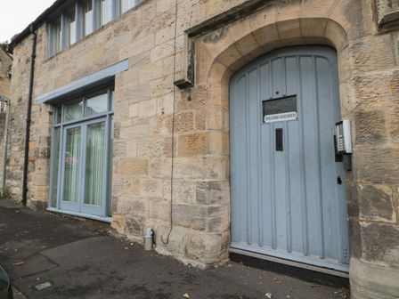 A stone building exterior with a blue arched door labeled Tomlinsons Apartments and a large window at The Coquet Nest in Rothbury