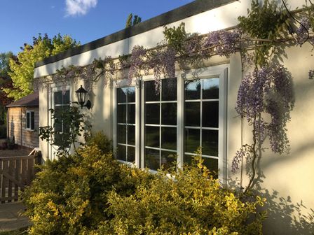 The exterior of a house with a window and a door surrounded by yellow bushes and purple flowers at October House Holiday Cabin in Damerham