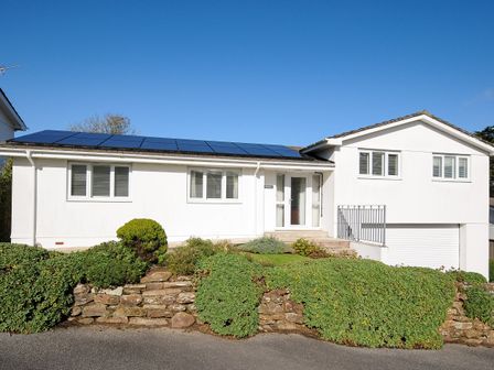 A white house with solar panels on the roof and bushes in front at Trestar in Polzeath