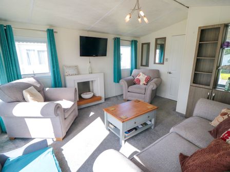 A living room with grey armchairs and sofa a wooden coffee table a wall-mounted TV and blue curtains at 13 Gosling in Cayton Bay