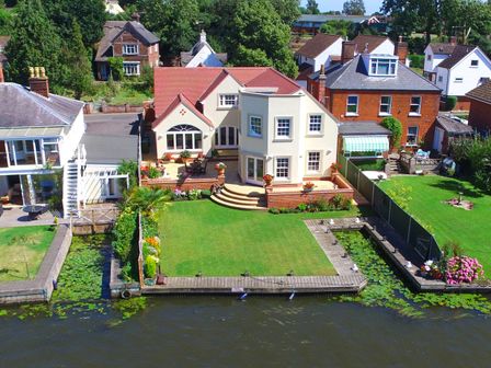 A riverside house with a lawn and flower pots on the patio at The Little House in Horning