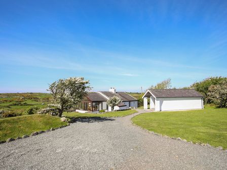 A gravel driveway leading to a white house and a separate white garage with grass and trees around at Ty Mynydd in Rhoscolyn
