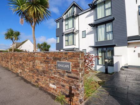 A residential building with multiple windows beside a stone wall with a seascape sign and palm trees