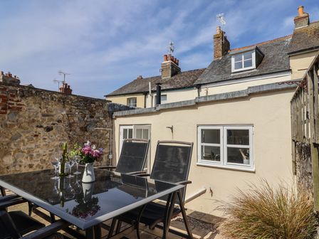 An outdoor patio area with a glass table and black chairs with flowers and wine glasses at 47 Church Street in Lyme Regis
